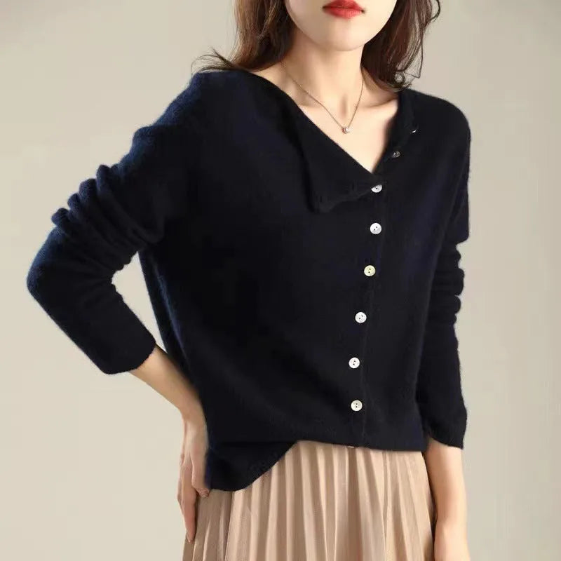 Navy blue cardigan with relaxed sleeves worn open at the collar over a beige pleated skirt