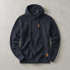 Navy basket-weave pullover hoodie laid flat, showing textured knit, lined hood and tan drawstring toggles