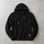 Black basket-weave knit hoodie laid flat with tan drawstring cord ends and ribbed trims