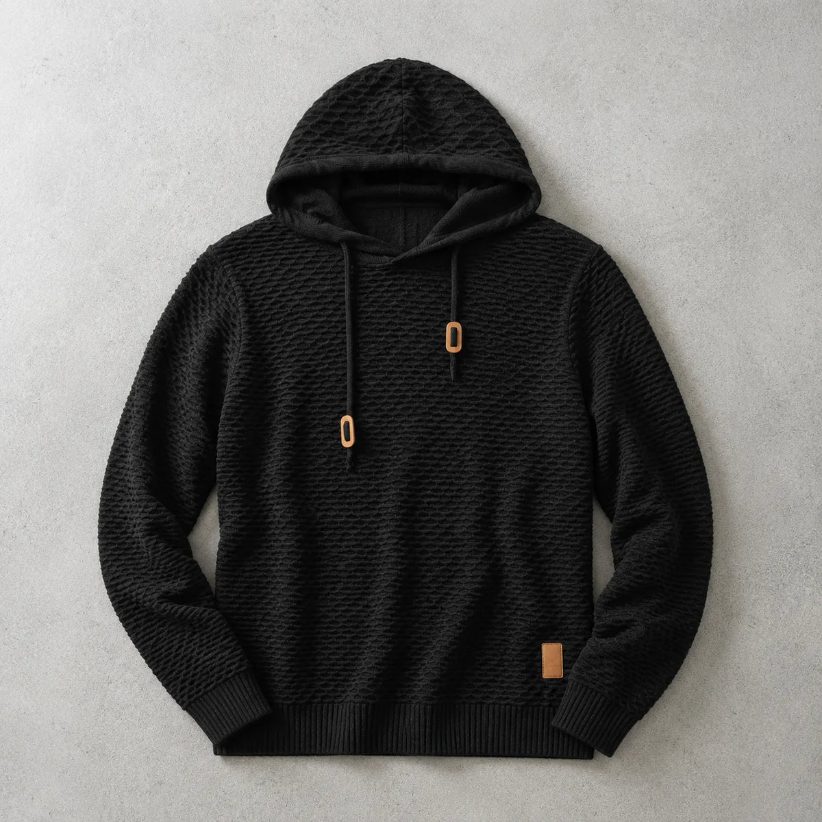 Black basket-weave knit hoodie laid flat with tan drawstring cord ends and ribbed trims