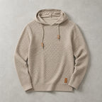 Beige knitted pullover hoodie laid flat, showing the raised basket-weave pattern and leather patch