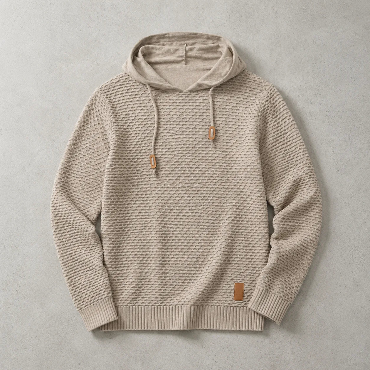 Beige knitted pullover hoodie laid flat, showing the raised basket-weave pattern and leather patch