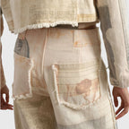Close-up back view of frayed patch pockets with faded sketch and line motifs on beige fabric