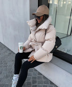 Woman seated wearing a cream puffer jacket tied at the waist, paired with black leggings and trainers