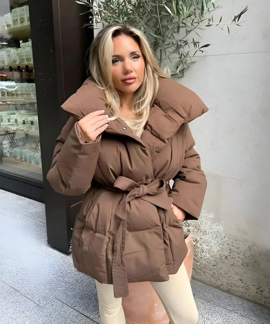 Brown belted puffer jacket with a large stand-up collar, worn open over a light top