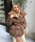 Brown belted puffer jacket with a large stand-up collar, worn open over a light top