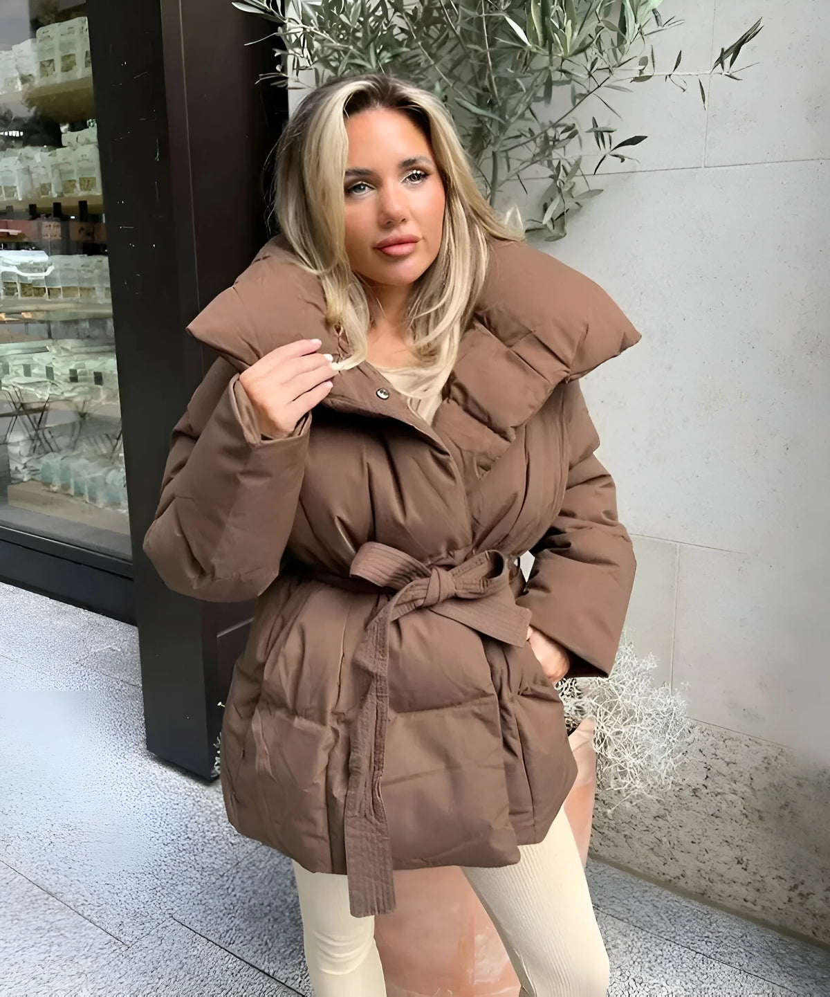 Brown belted puffer jacket with a large stand-up collar, worn open over a light top