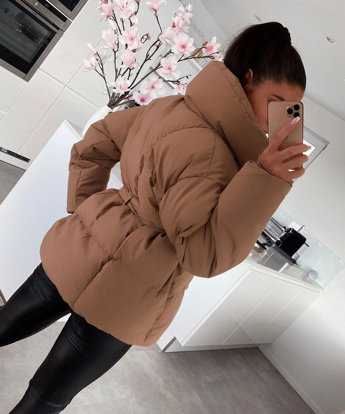Close side view of a brown puffer jacket showing the quilted panels and tied belt detail