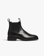 Side profile of a black calf leather Chelsea boot with elastic side panel, pull tab and stitched apron toe on a low block heel