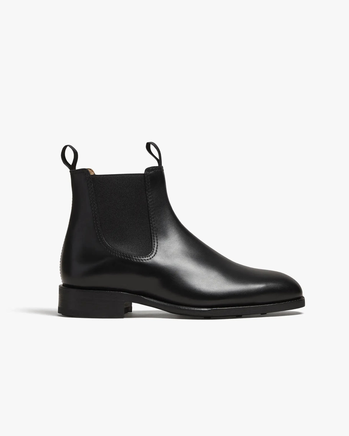 Side profile of a black calf leather Chelsea boot with elastic side panel, pull tab and stitched apron toe on a low block heel