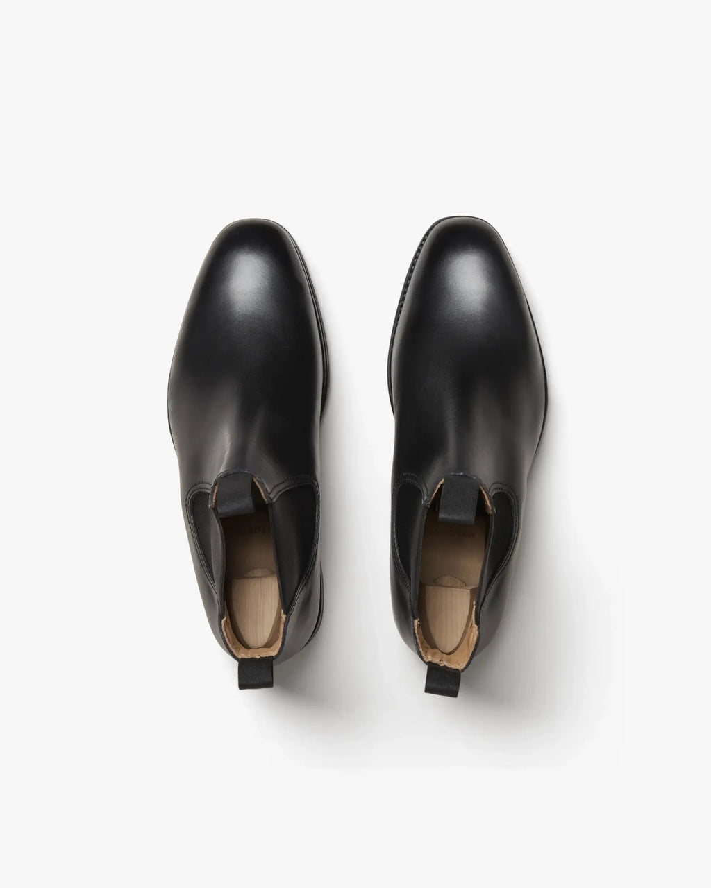 Overhead view of a matched pair of black leather Chelsea boots fitted with wooden shoe trees to show shape and elastic gussets