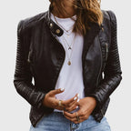 Front view of a cropped black faux leather biker jacket worn open over a white t-shirt and layered gold necklaces
