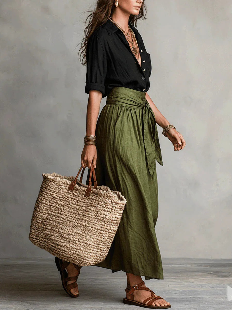 Side profile view of the black shirt tucked into the belted olive green skirt with layered gold necklaces