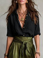 Close-up of the black button-up shirt collar with layered gold necklaces and bracelets