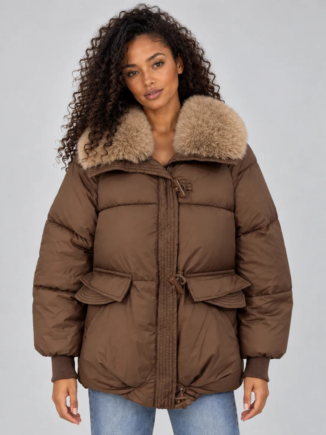 Front view of brown padded puffer jacket with plush faux fur collar, zip and toggle fastening, worn over jeans