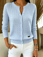 Light blue cable knit cardigan with buttons undone at the neckline, worn with white trousers and a necklace