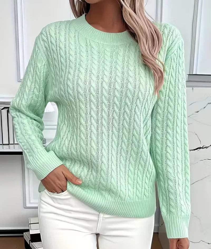 Front view of mint green cable-knit crew-neck jumper with ribbed cuffs, worn with white trousers