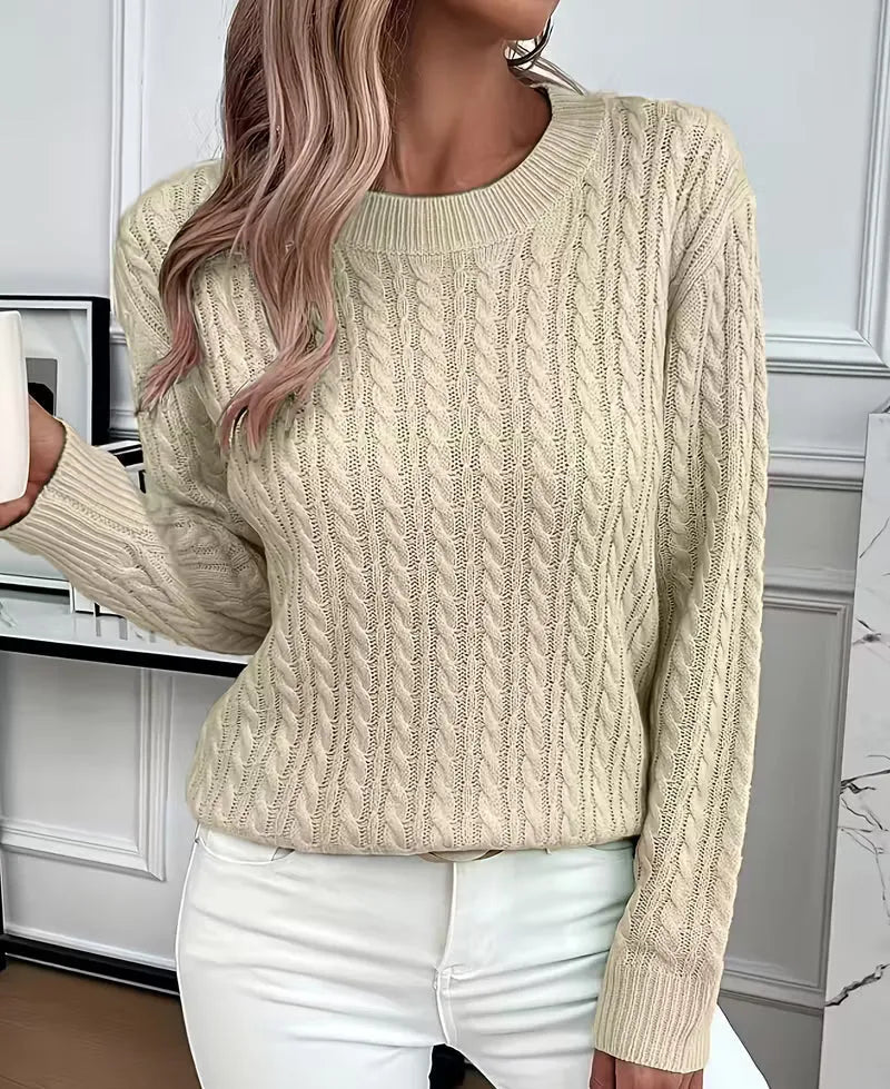 Beige cable-knit jumper worn while holding a mug, showing ribbed cuff and sleeve detail