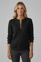 Woman wearing a black cable knit zip-neck jumper with long sleeves, styled with a gold chain necklace
