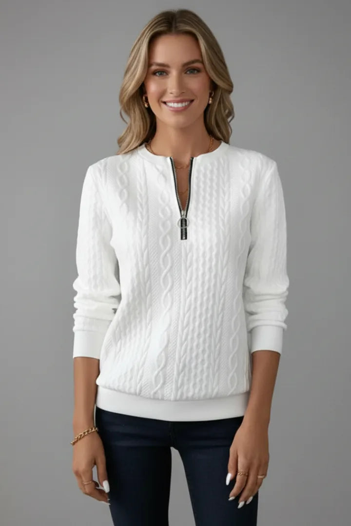 Front view of a white cable knit jumper with a zip neckline, worn with dark denim trousers
