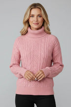 Front view of a pink cable knit jumper with a folded polo neck collar, worn with black trousers