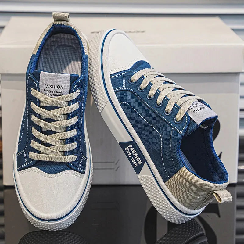 Pair of blue canvas trainers with cream laces and contrast heel panel, shown resting against the shoebox