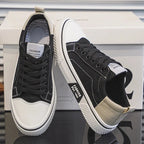 Black and white canvas trainers with woven laces, paired upright next to the shoebox