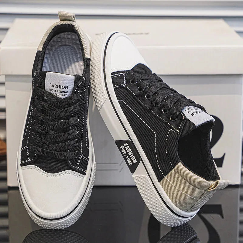 Black and white canvas trainers with woven laces, paired upright next to the shoebox