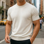 Close-up of a man wearing an ivory white short-sleeve knitted T-shirt with ribbed crew neck on a city street