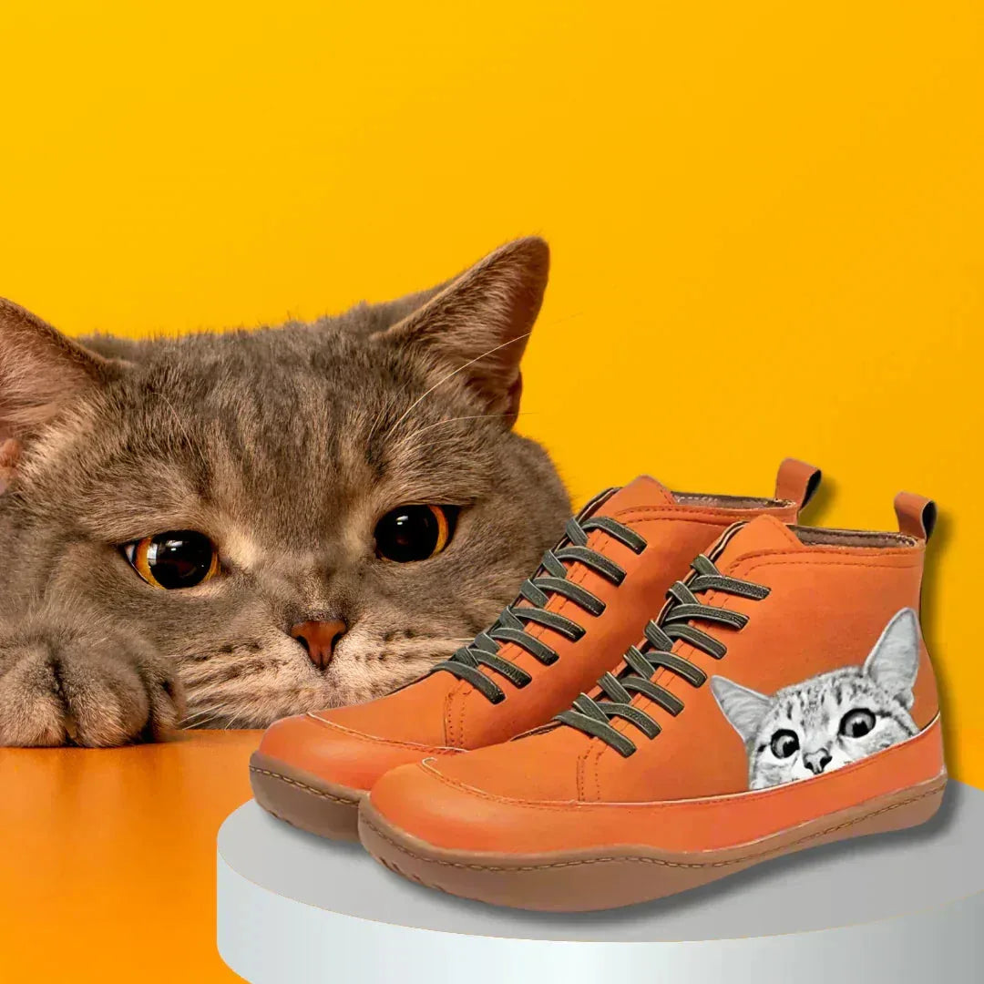 Orange boots styled against a yellow backdrop beside a grey tabby cat, highlighting the matching peeking cat print