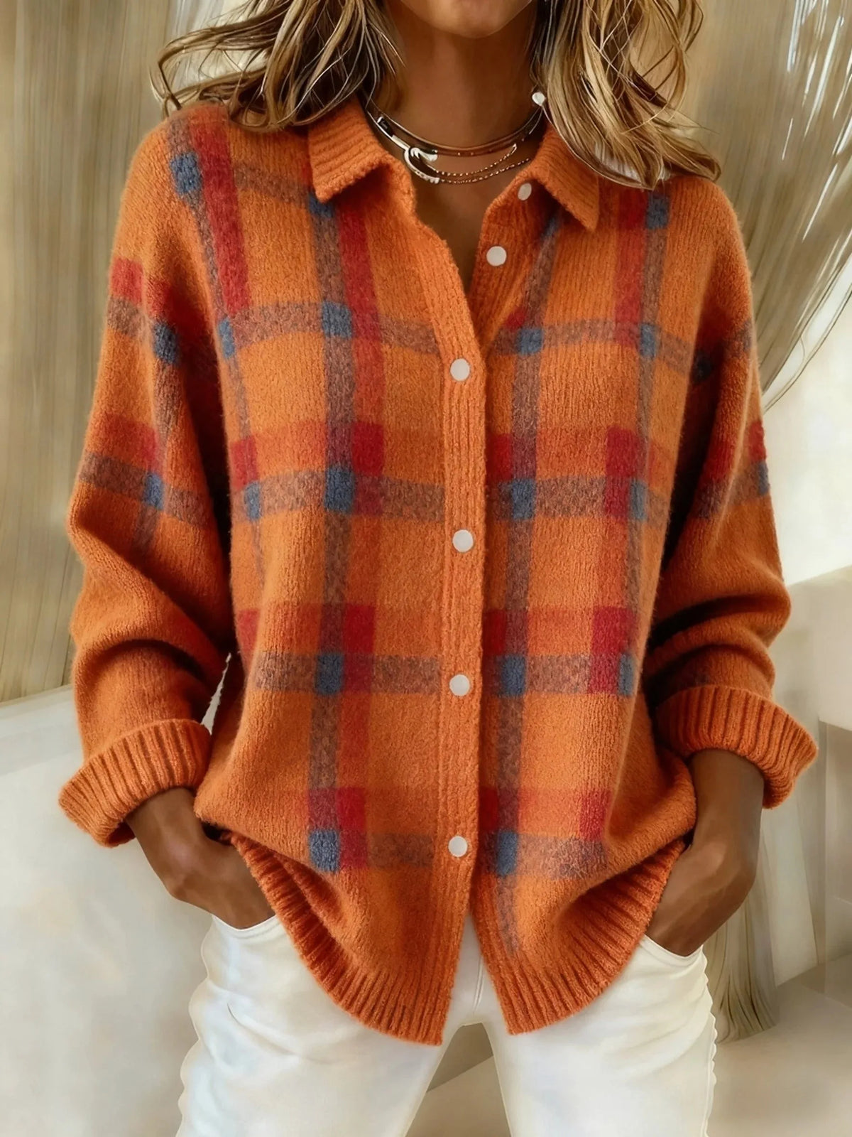 Close-up of orange checked knit shacket with white button fastenings and collared neckline, worn over white trousers
