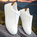 Pair of white perforated trainers with tan accent displayed on a rock with a mountain sunset backdrop
