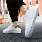 Close-up of a white trainer with tan heel tab worn on foot mid-step on a city street