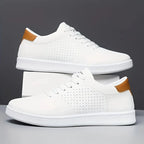 Pair of white trainers with tan heel trim and perforated detailing stacked on a white box