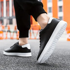 Close-up of a black trainer with white heel tab worn on foot mid-step on a city pavement