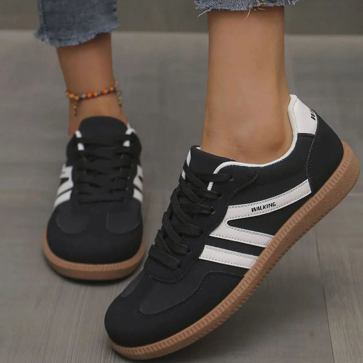 Front view of black trainers with white stripes and gum sole worn on feet