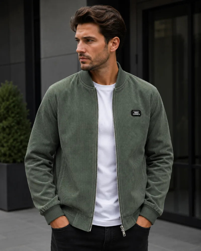 Man wearing an olive green corduroy bomber jacket with ribbed collar and cuffs, zipped over a white t-shirt.