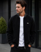 Black corduroy bomber jacket with contrast grey ribbed collar, zipped fully over a white tee.