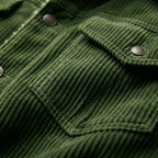 Close-up of green corduroy jacket chest pocket with antique metal snap button and visible stitched seams