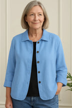 Woman wearing an open light blue cotton-linen shirt jacket with three-quarter sleeves over a black top and jeans