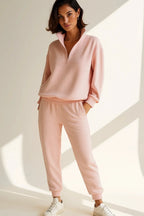 Front view of woman wearing a pink half-zip sweatshirt and matching jogger trousers with white trainers