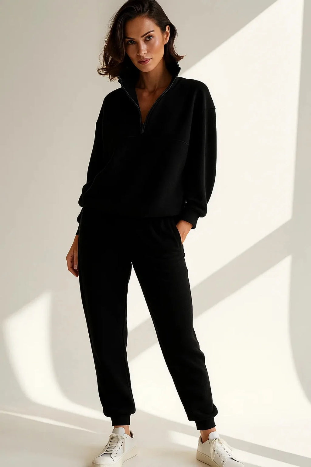 Woman wearing the same tracksuit style in black with a zip-up funnel collar and tapered joggers