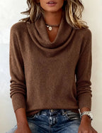 Close-up of a brown cowl neck jumper with long sleeves and ribbed cuffs, layered necklaces visible at the neckline