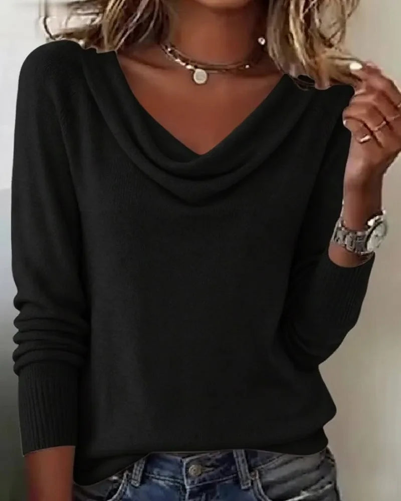Dark purple cowl neck jumper worn with hands resting at the waist over denim trousers