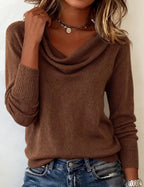 Brown cowl neck jumper worn with hand raised to collar, showing ribbed sleeve cuff detail