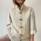 Close-up of a cream chunky knit gilet with wooden toggle buttons worn over a light beige linen shirt
