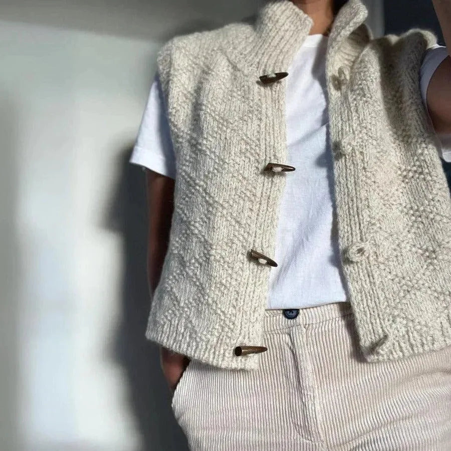 Side view of the cream knitted gilet with high stand collar, wooden toggles, and diamond stitch pattern