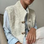 Cream textured knit gilet layered over a light blue shirt, showing the ribbed collar and hem detail