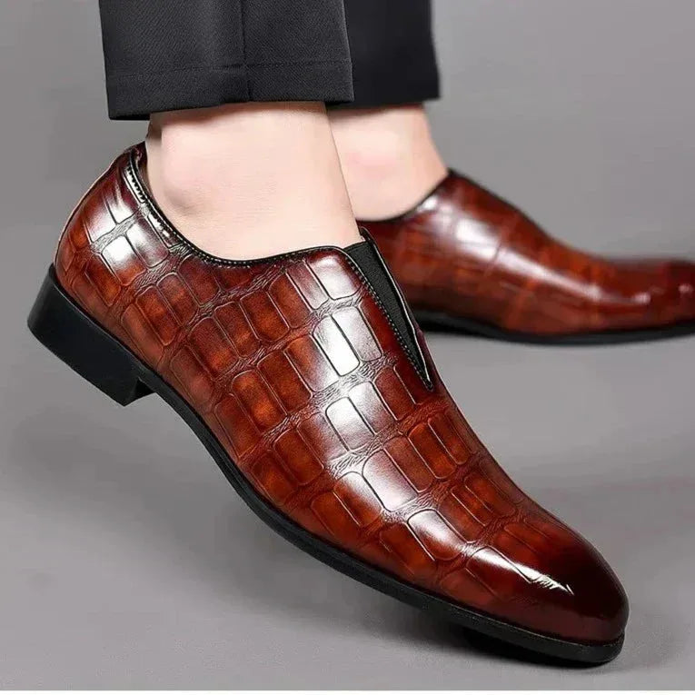 Side view of a model wearing dark brown croc-textured loafers with tapered trousers, showing the low block heel