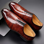 Top-down view of a pair of dark brown croc-embossed loafers resting on a dark reflective surface